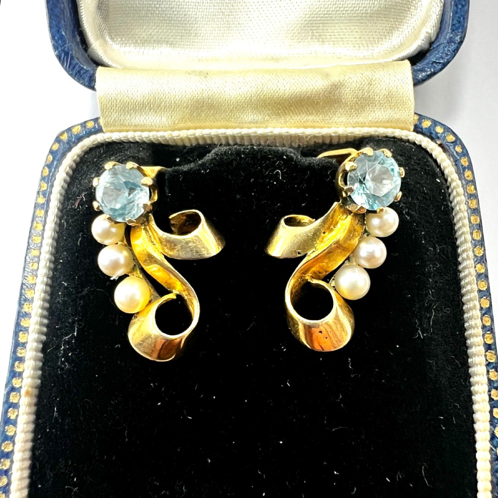 A pair of 1940s 9ct yellow gold ear clips featuring faceted round blue zircons and graduated pearls set against curved ribbon scrollwork.
