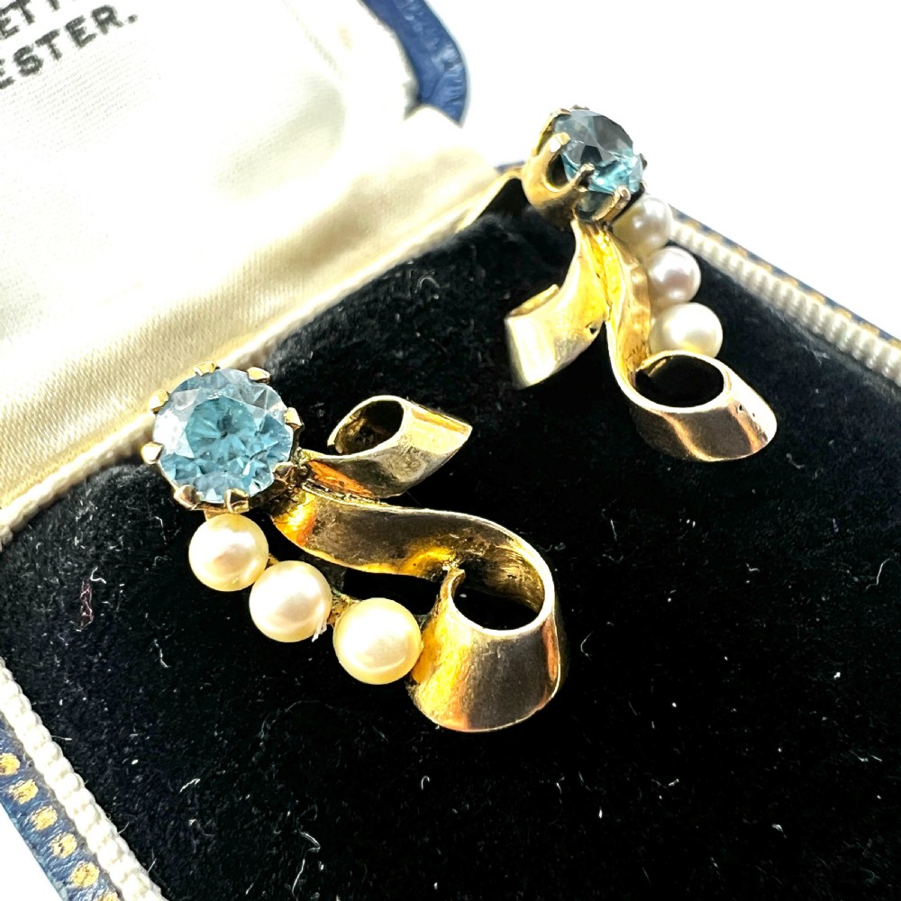 A pair of 1940s 9ct yellow gold ear clips featuring faceted round blue zircons and graduated pearls set against curved ribbon scrollwork. View II