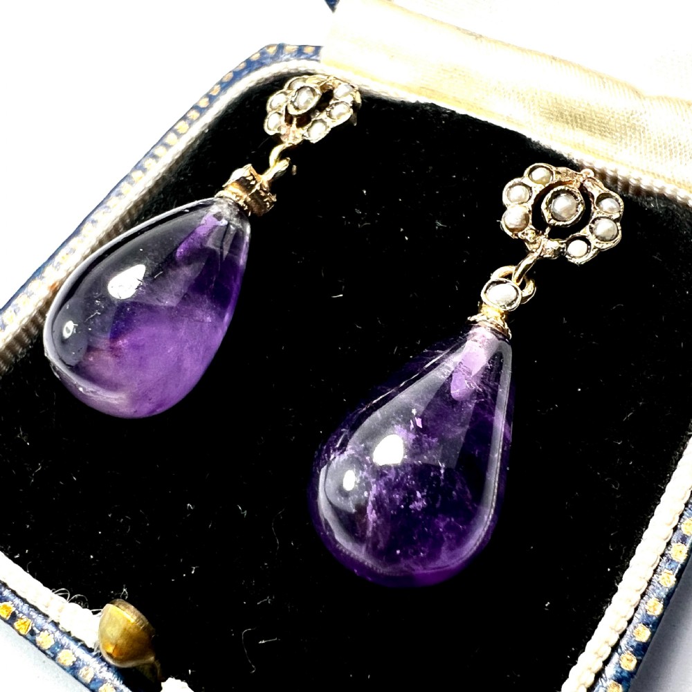 A pair of Victorian gold drop earrings featuring teardrop cabochon amethysts suspended from pearl-set floral clusters inside a fitted velvet box. View II