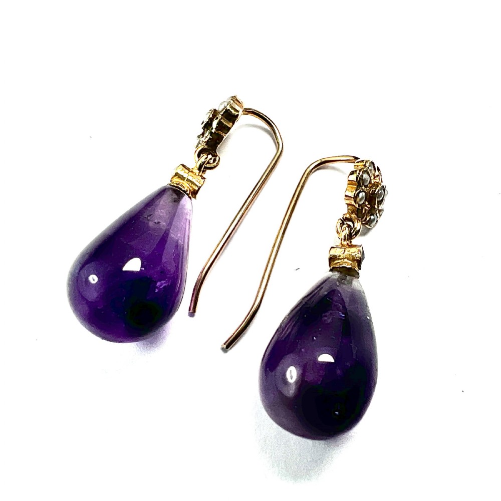 A pair of Victorian gold drop earrings featuring teardrop cabochon amethysts suspended from pearl-set floral clusters inside a fitted velvet box. View V
