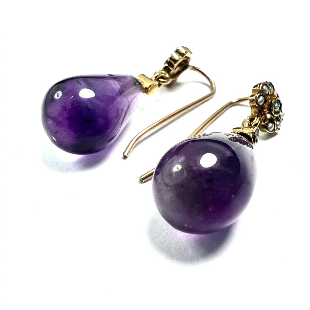 A pair of Victorian gold drop earrings featuring teardrop cabochon amethysts suspended from pearl-set floral clusters inside a fitted velvet box. View VI