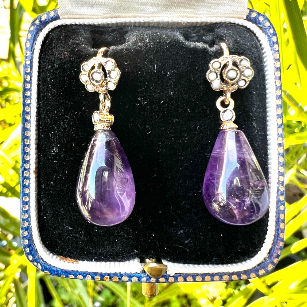 A pair of Victorian gold drop earrings featuring teardrop cabochon amethysts suspended from pearl-set floral clusters inside a fitted velvet box. View IX