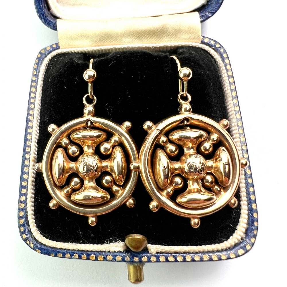 A pair of Victorian 9ct yellow gold drop earrings featuring a circular wheel design with a central square cross motif.