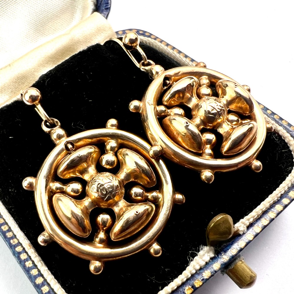 A pair of Victorian 9ct yellow gold drop earrings featuring a circular wheel design with a central square cross motif. View II