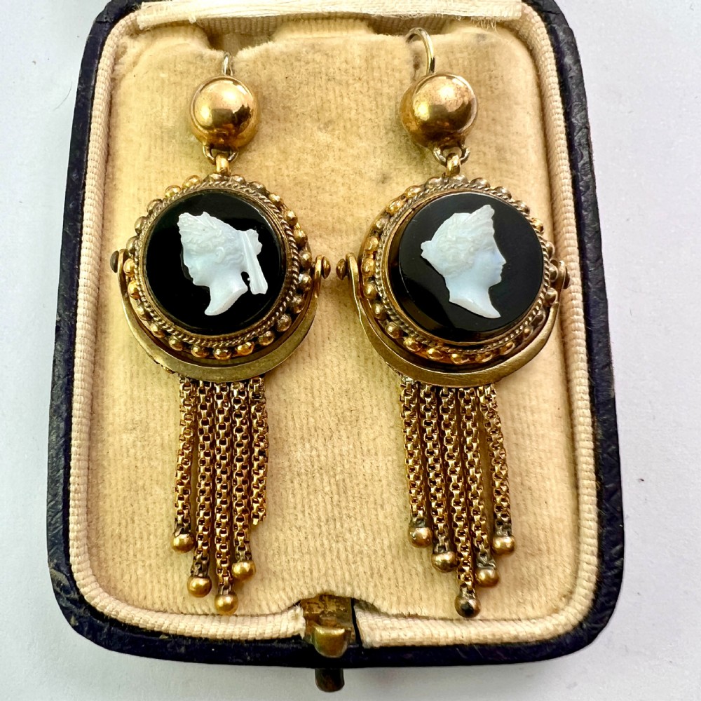 A pair of Victorian gold drop earrings featuring carved classical profile cameos mounted on black discs with cascading foxtail chain tassels.