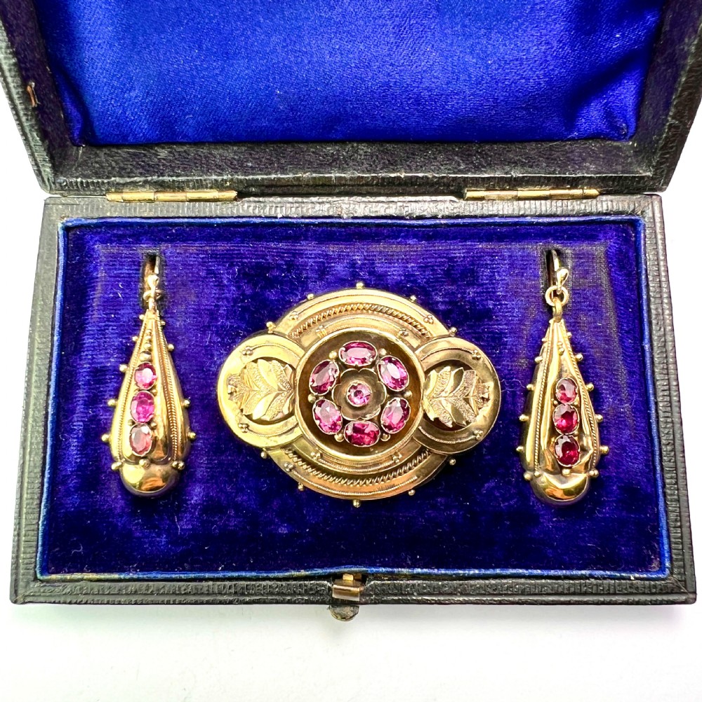 A Victorian gold demi parure set featuring an ornate oval brooch and matching drop earrings inset with amethysts, presented inside a blue velvet-lined case.