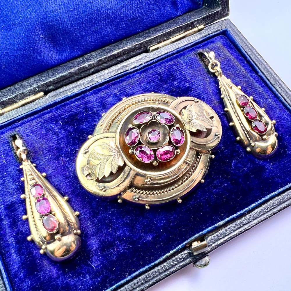 A Victorian gold demi parure set featuring an ornate oval brooch and matching drop earrings inset with amethysts, presented inside a blue velvet-lined case. View II