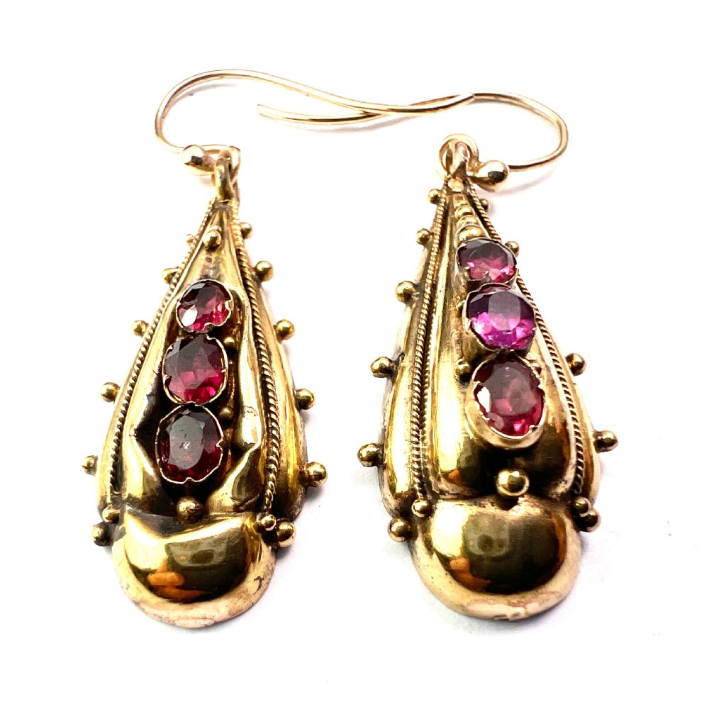 A Victorian gold demi parure set featuring an ornate oval brooch and matching drop earrings inset with amethysts, presented inside a blue velvet-lined case. View V