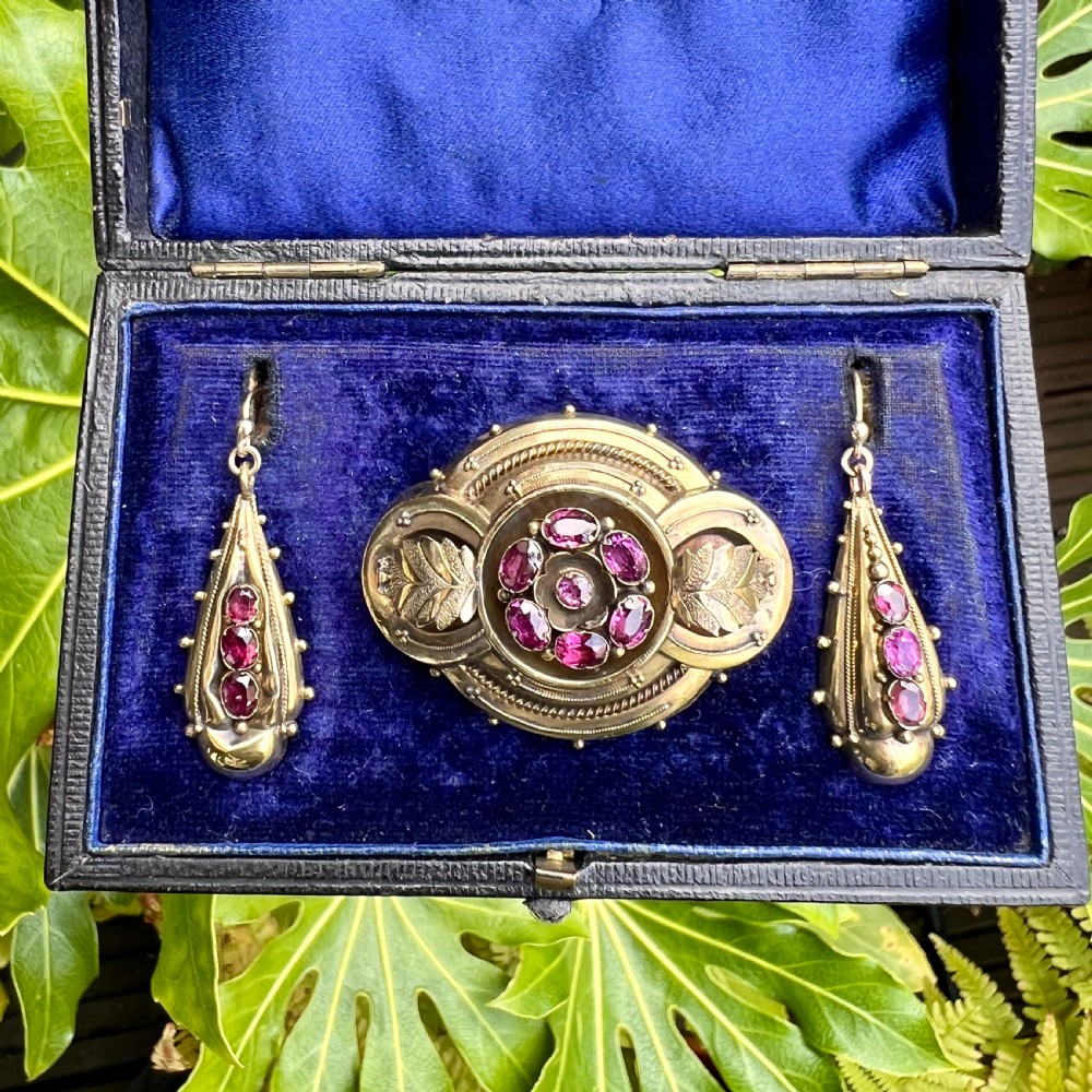 A Victorian gold demi parure set featuring an ornate oval brooch and matching drop earrings inset with amethysts, presented inside a blue velvet-lined case. View VII