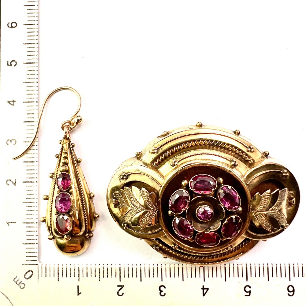 A Victorian gold demi parure set featuring an ornate oval brooch and matching drop earrings inset with amethysts, presented inside a blue velvet-lined case. View IX