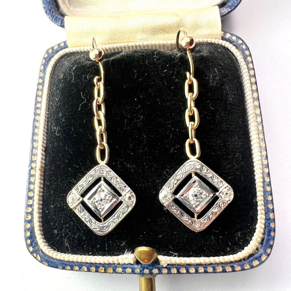 A pair of Edwardian style diamond drop earrings crafted in yellow and white gold with diamond-shaped engraved pendants.