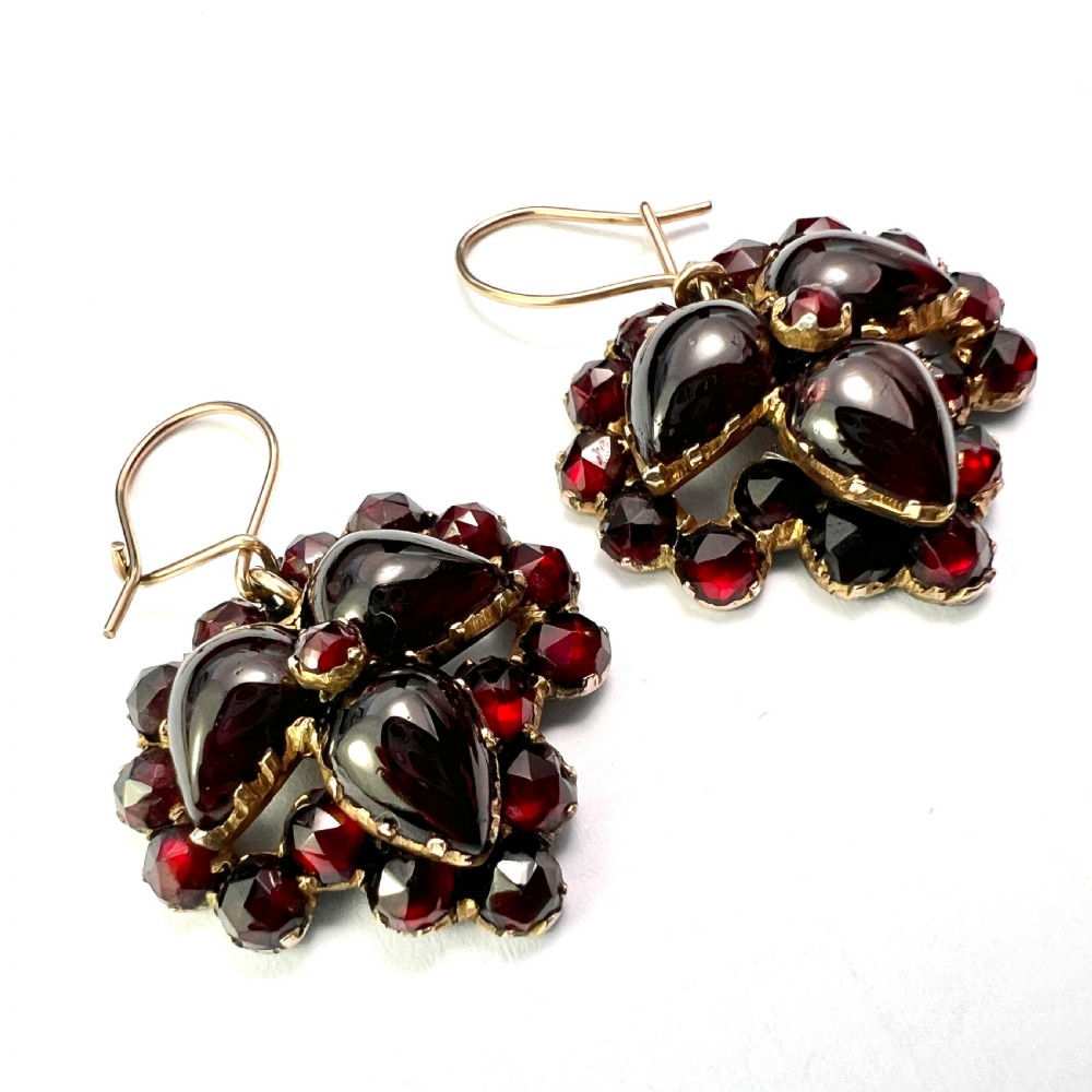 A pair of Victorian Bohemian garnet cluster drop earrings featuring cabochon central garnets surrounded by rose-cut pyrope garnets set on gold wire hooks.
