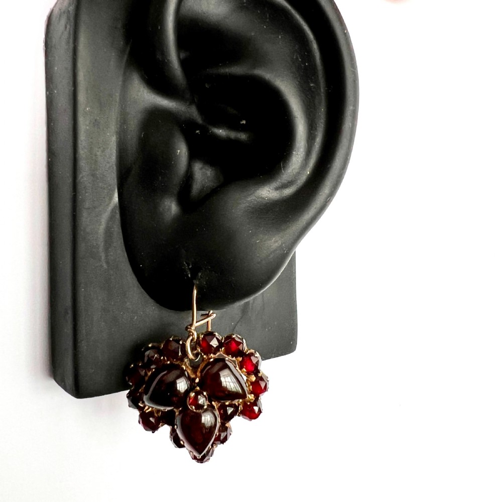 A pair of Victorian Bohemian garnet cluster drop earrings featuring cabochon central garnets surrounded by rose-cut pyrope garnets set on gold wire hooks. View VI