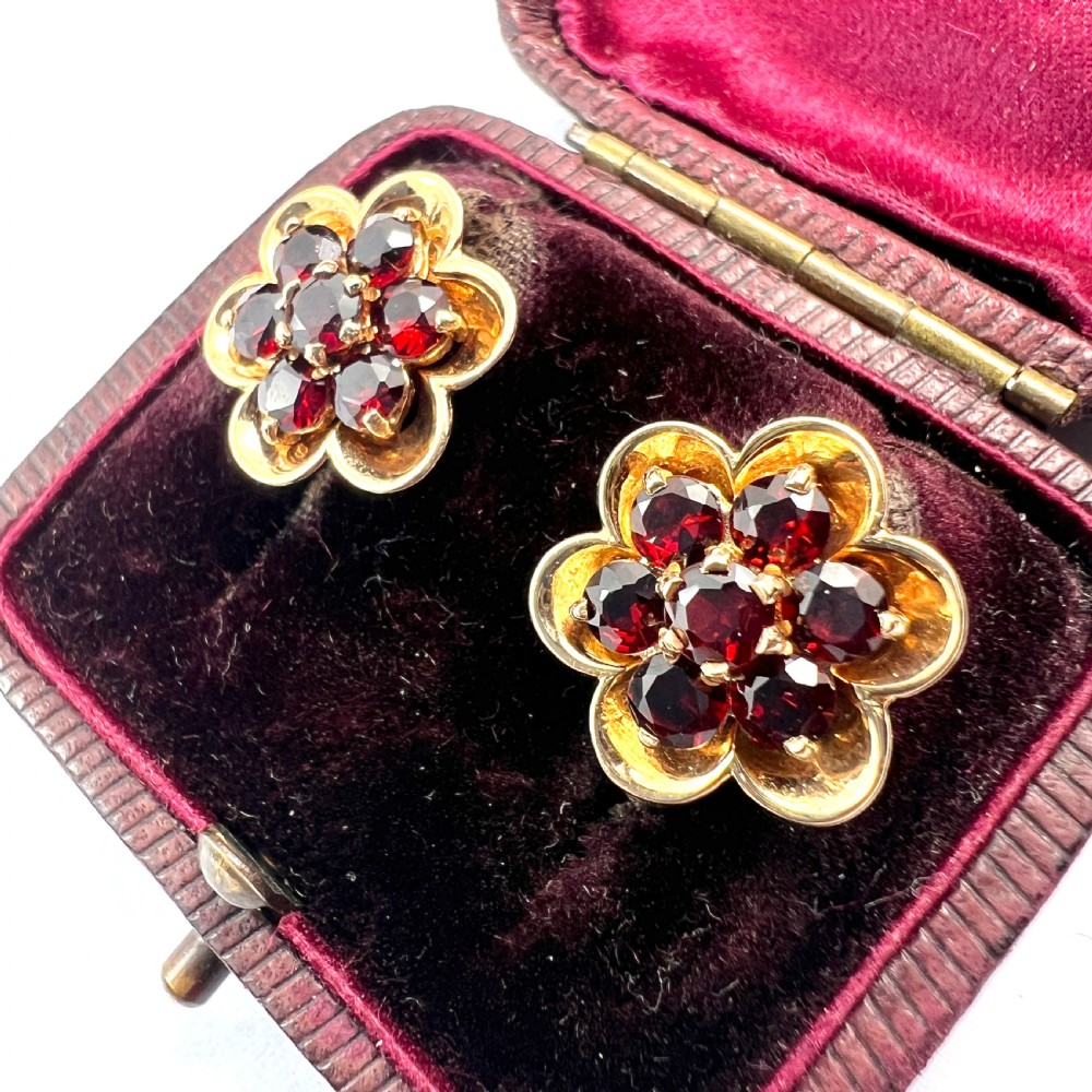 A pair of 9ct yellow gold floral cluster stud earrings set with round deep red garnet gemstones in claw settings.