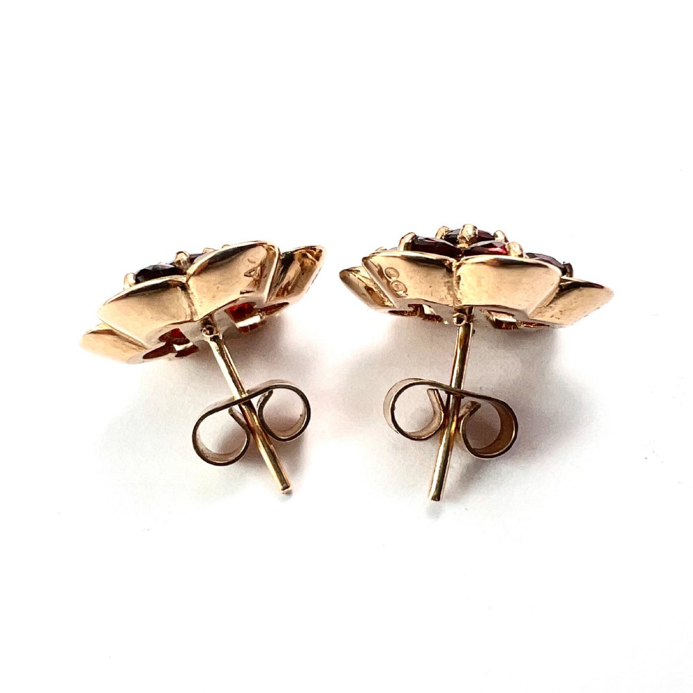 A pair of 9ct yellow gold floral cluster stud earrings set with round deep red garnet gemstones in claw settings. View VI