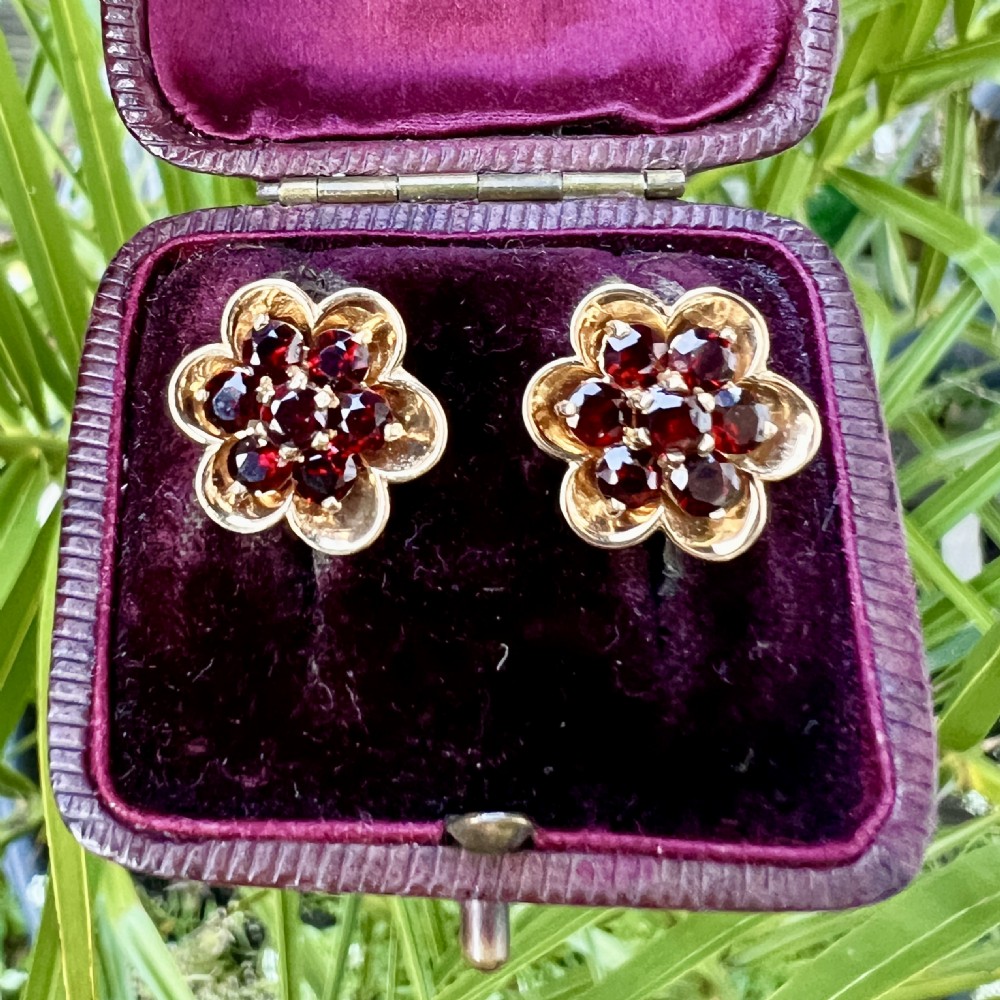 A pair of 9ct yellow gold floral cluster stud earrings set with round deep red garnet gemstones in claw settings. View X