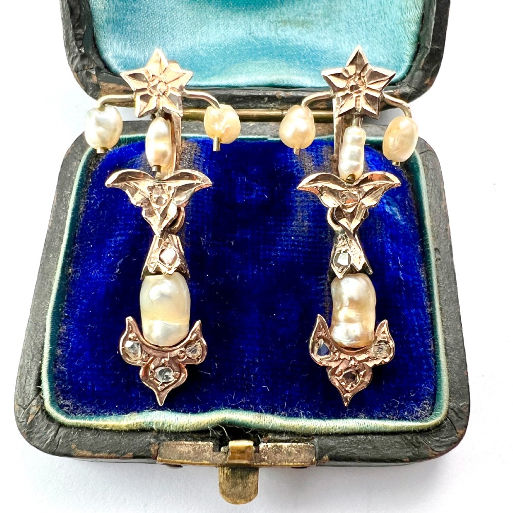 A pair of Art Nouveau gold drop earrings featuring star tops, leaf motifs set with small diamonds, and suspended baroque pearls.