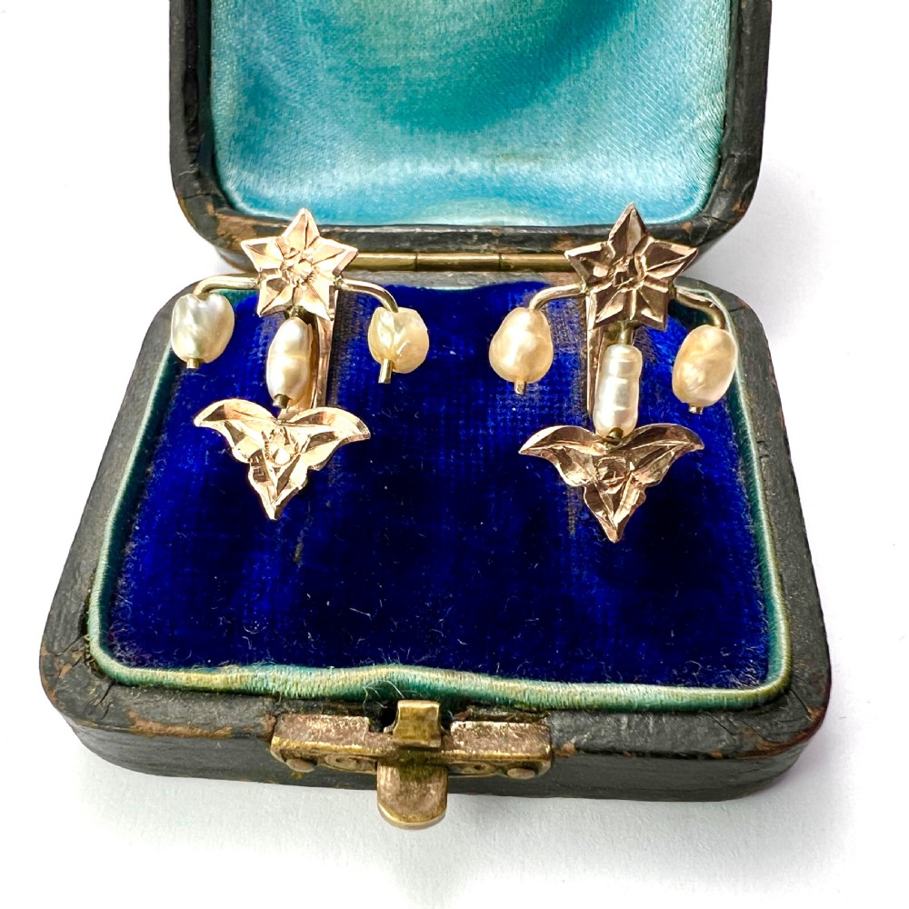 A pair of Art Nouveau gold drop earrings featuring star tops, leaf motifs set with small diamonds, and suspended baroque pearls. View V