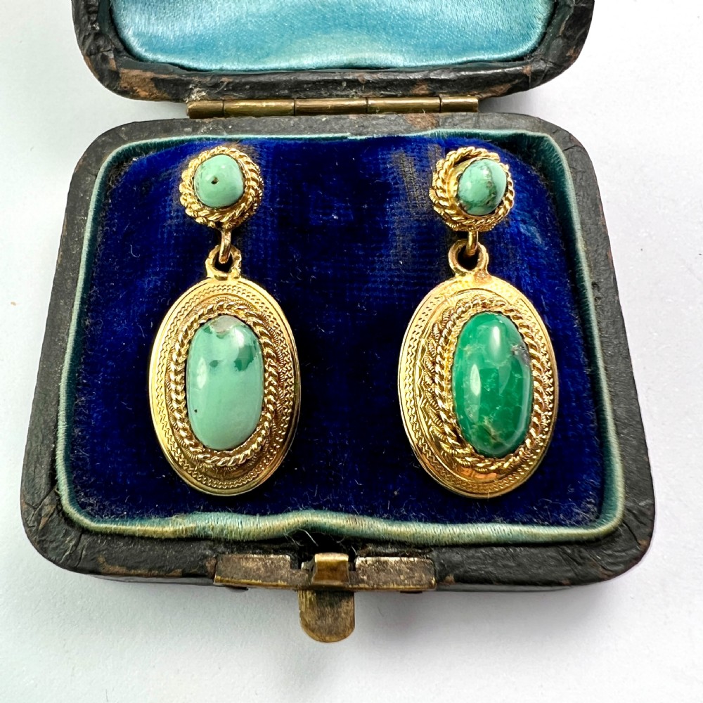A pair of Etruscan Revival drop earrings in yellow gold featuring oval cabochon turquoise stones with detailed ropework and granulation.
