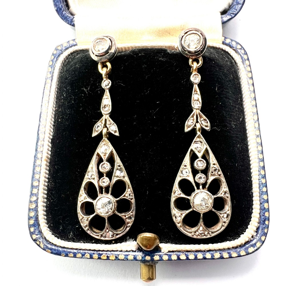 A pair of antique silver-topped gold drop earrings featuring openwork teardrop pendants set with old-cut diamonds, resting inside a blue fitted box.