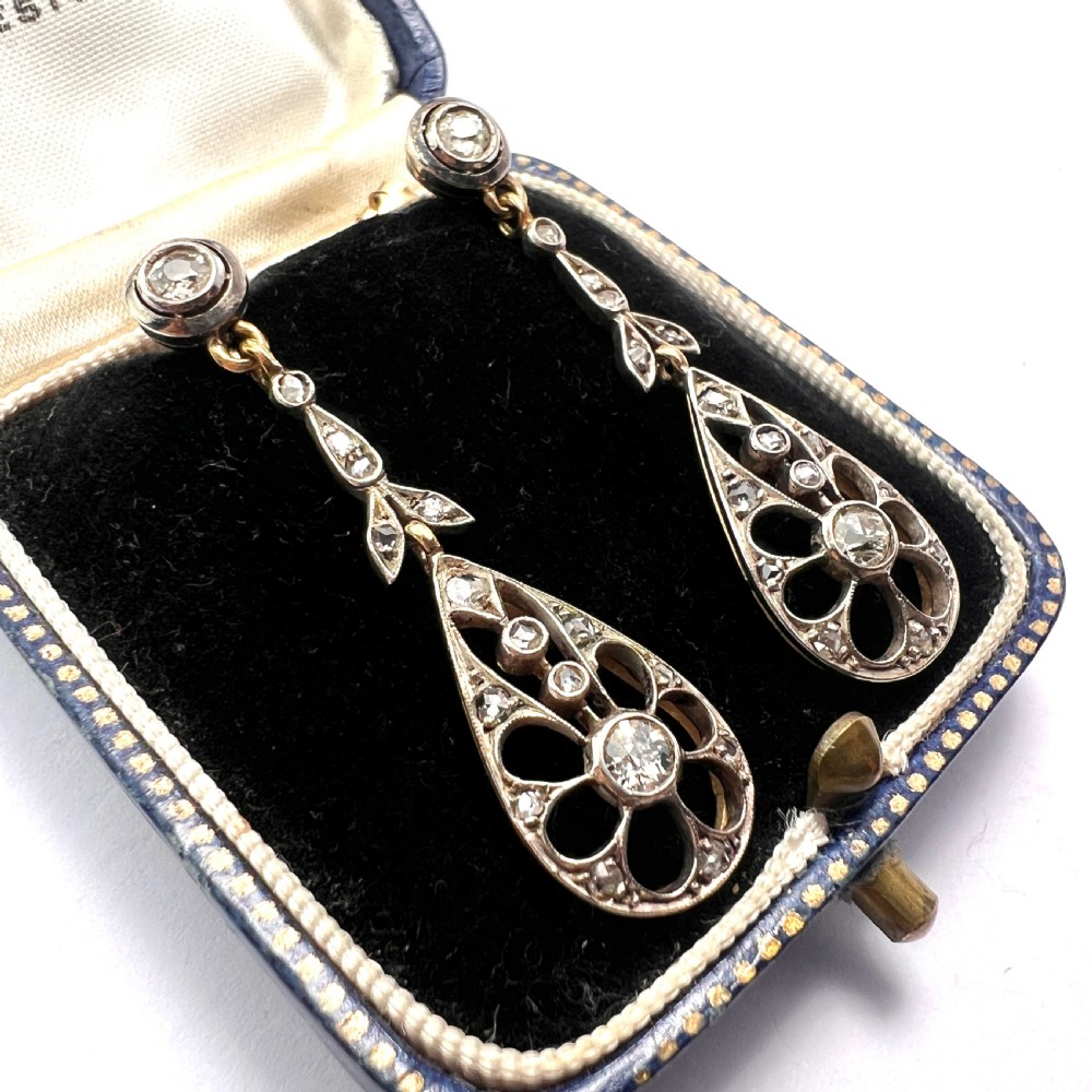 A pair of antique silver-topped gold drop earrings featuring openwork teardrop pendants set with old-cut diamonds, resting inside a blue fitted box. View II