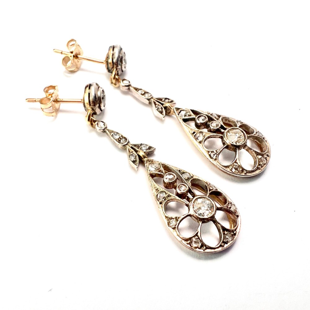 A pair of antique silver-topped gold drop earrings featuring openwork teardrop pendants set with old-cut diamonds, resting inside a blue fitted box. View IV