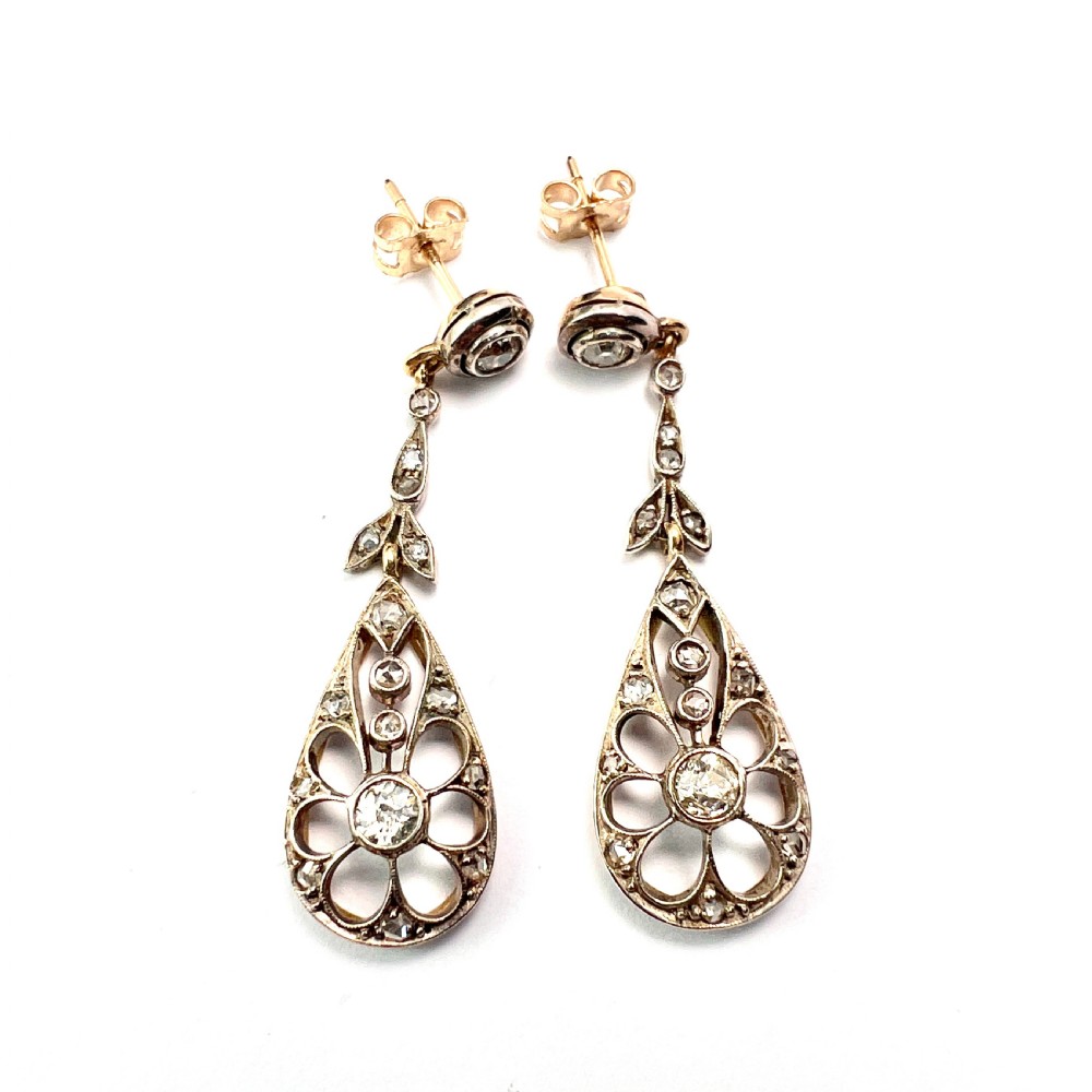 A pair of antique silver-topped gold drop earrings featuring openwork teardrop pendants set with old-cut diamonds, resting inside a blue fitted box. View V