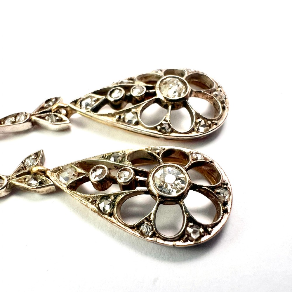 A pair of antique silver-topped gold drop earrings featuring openwork teardrop pendants set with old-cut diamonds, resting inside a blue fitted box. View VI