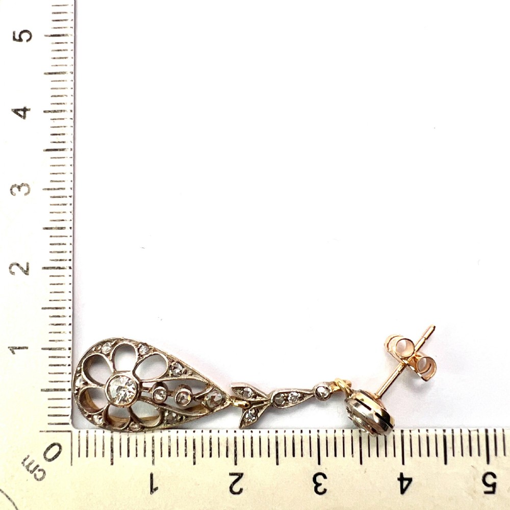 A pair of antique silver-topped gold drop earrings featuring openwork teardrop pendants set with old-cut diamonds, resting inside a blue fitted box. View VII
