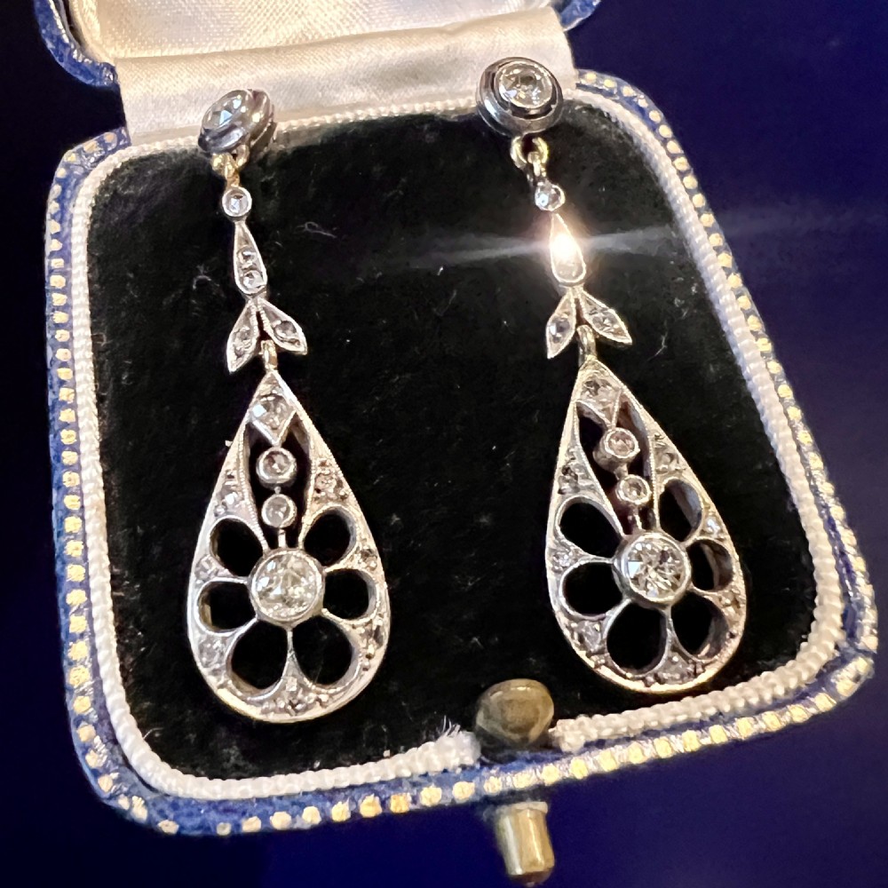 A pair of antique silver-topped gold drop earrings featuring openwork teardrop pendants set with old-cut diamonds, resting inside a blue fitted box. View VIII