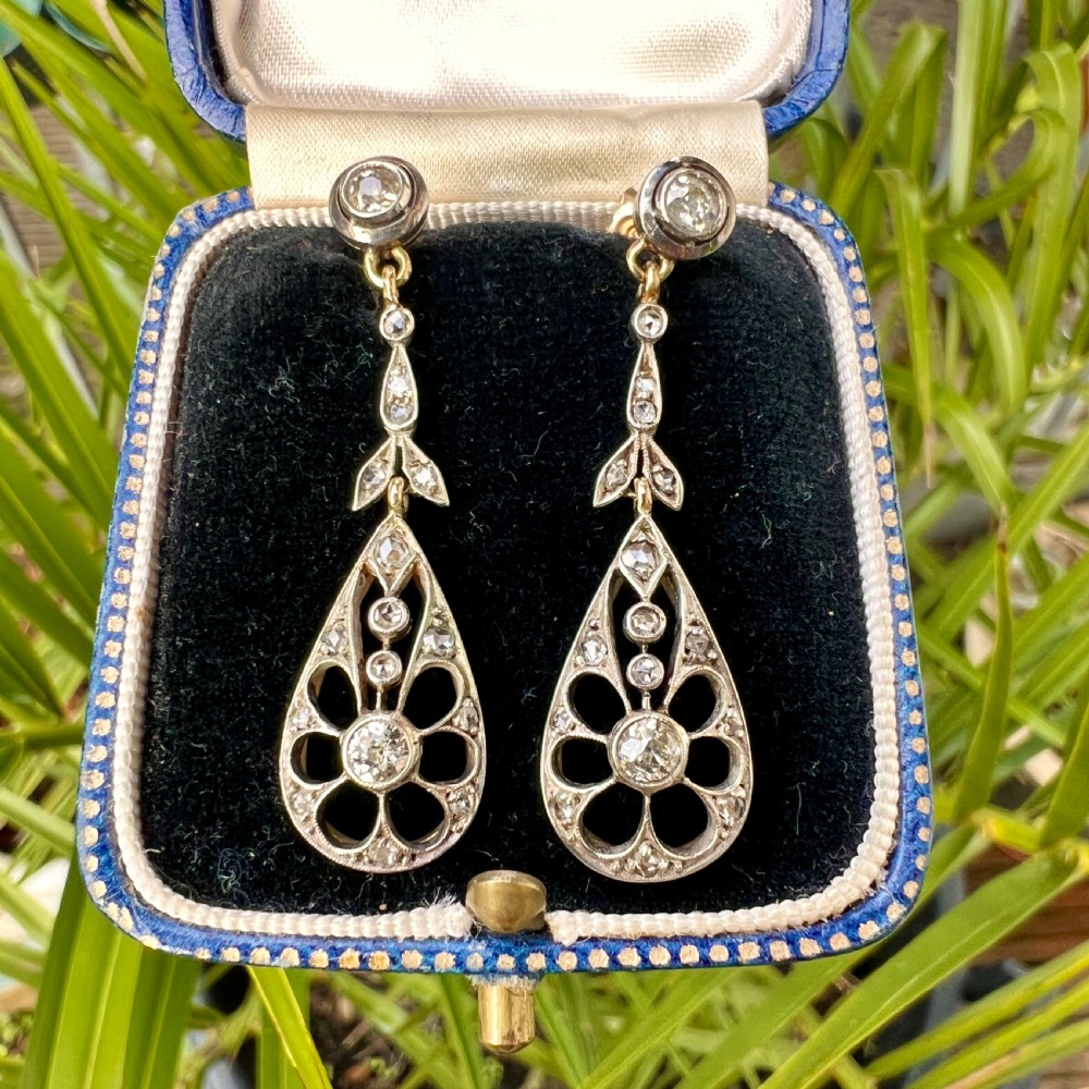 A pair of antique silver-topped gold drop earrings featuring openwork teardrop pendants set with old-cut diamonds, resting inside a blue fitted box. View IX
