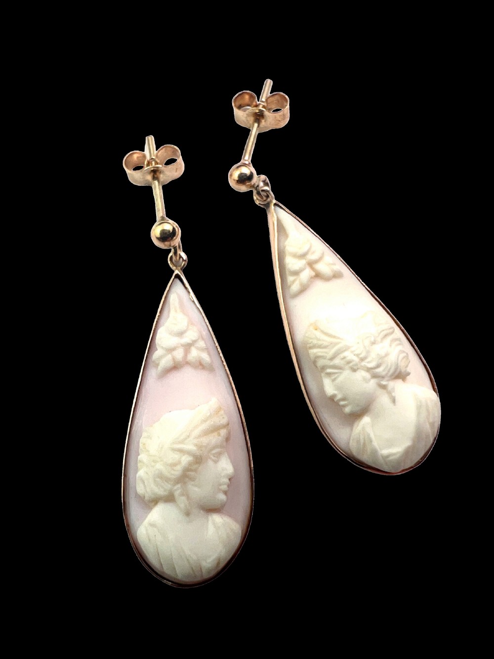 A pair of teardrop-shaped 9ct gold drop earrings featuring carved shell cameos with classical profile portraits set against a pink shell background.