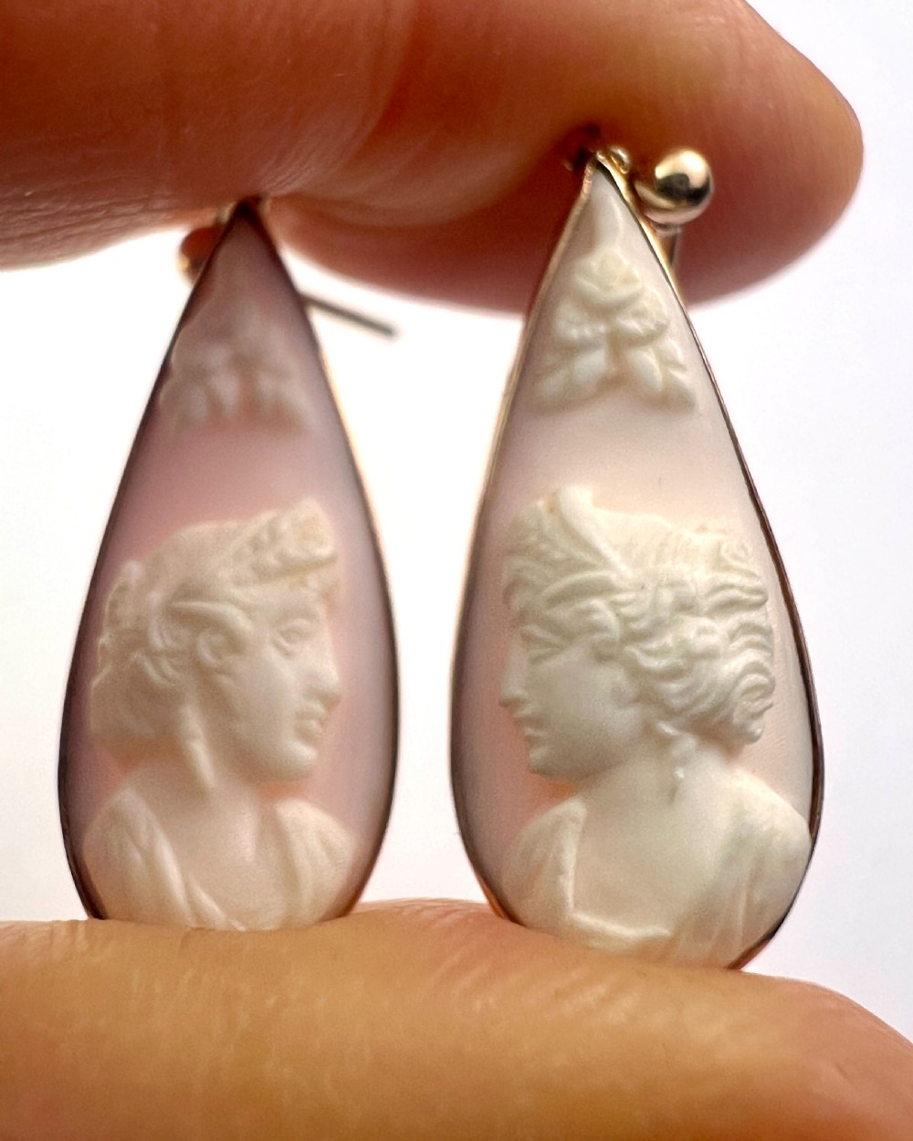 A pair of teardrop-shaped 9ct gold drop earrings featuring carved shell cameos with classical profile portraits set against a pink shell background. View IV