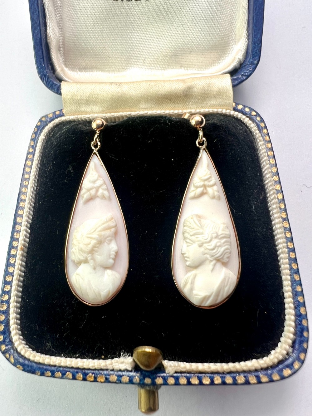 A pair of teardrop-shaped 9ct gold drop earrings featuring carved shell cameos with classical profile portraits set against a pink shell background. View V