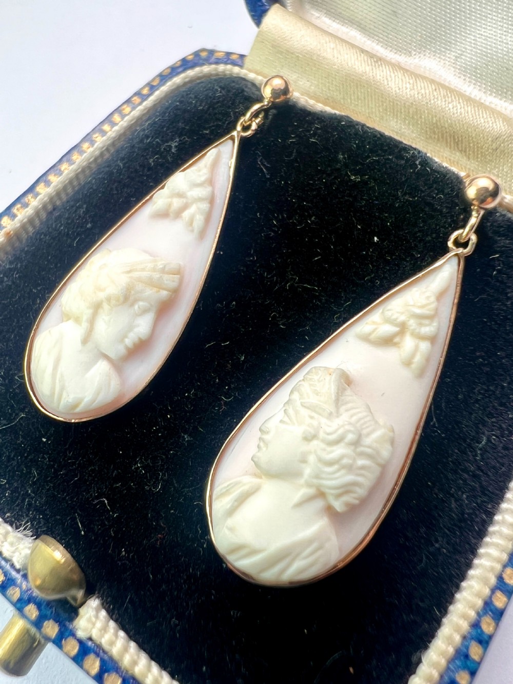 A pair of teardrop-shaped 9ct gold drop earrings featuring carved shell cameos with classical profile portraits set against a pink shell background. View VI