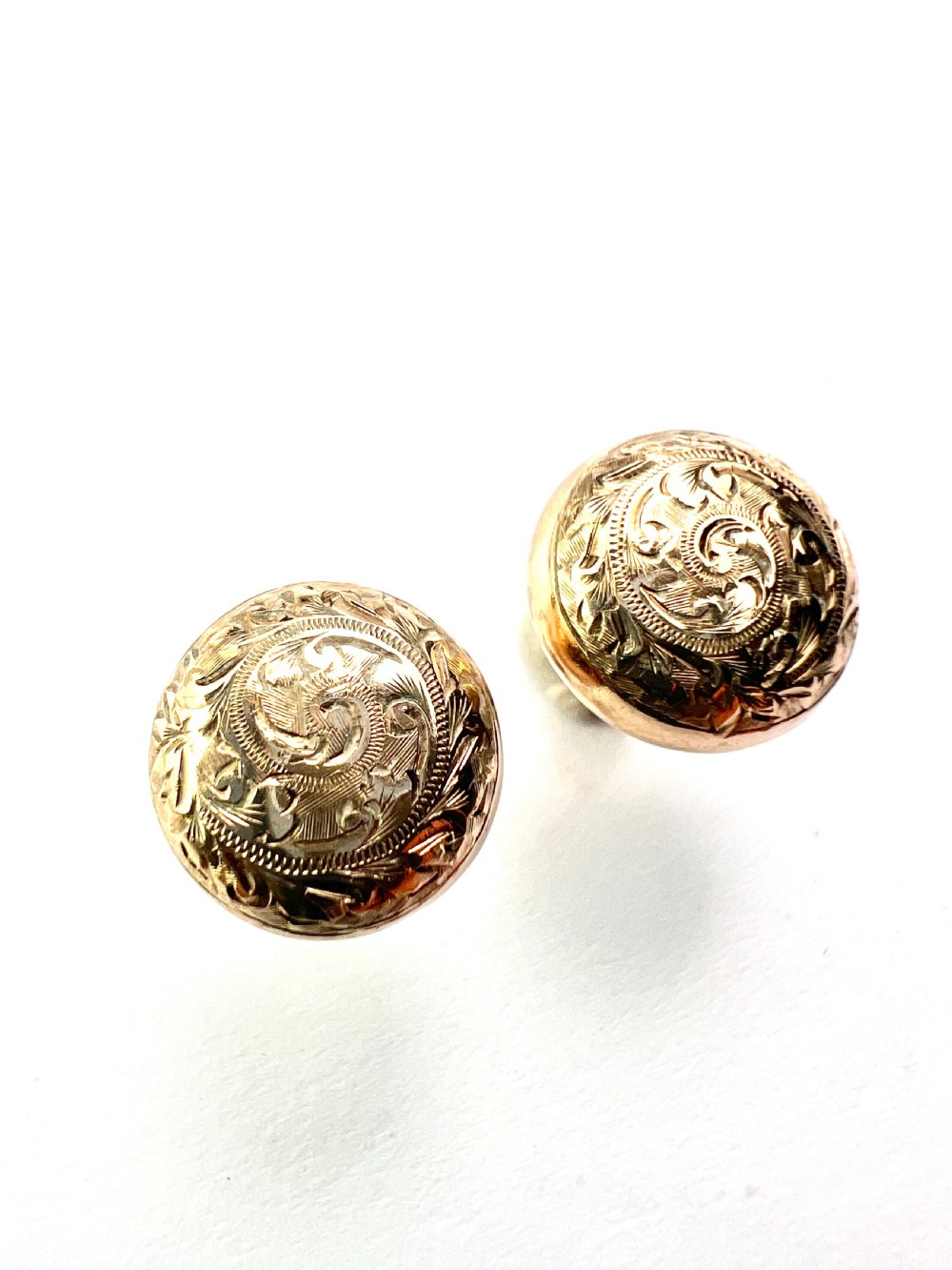 A pair of circular domed yellow gold stud earrings featuring hand-engraved scrollwork across the surface.