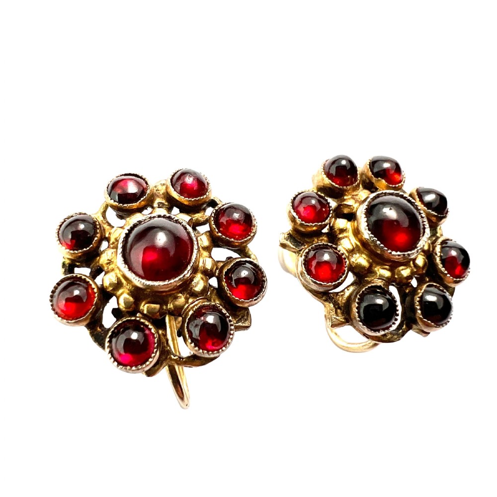 A pair of antique silver-gilt earrings set with deep red cabochon garnets arranged in a circular cluster halo design.