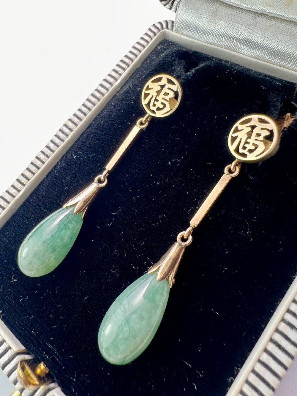 A pair of gold drop earrings featuring circular tops with pierced Chinese characters, slender gold bar links, and teardrop-shaped green jade stones. View II