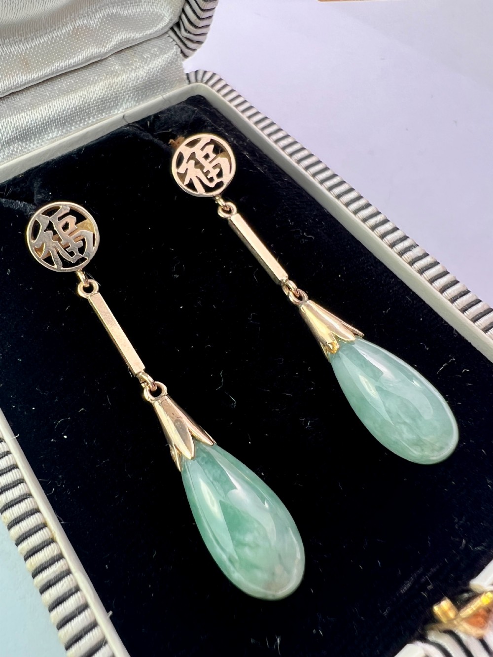 A pair of gold drop earrings featuring circular tops with pierced Chinese characters, slender gold bar links, and teardrop-shaped green jade stones. View III