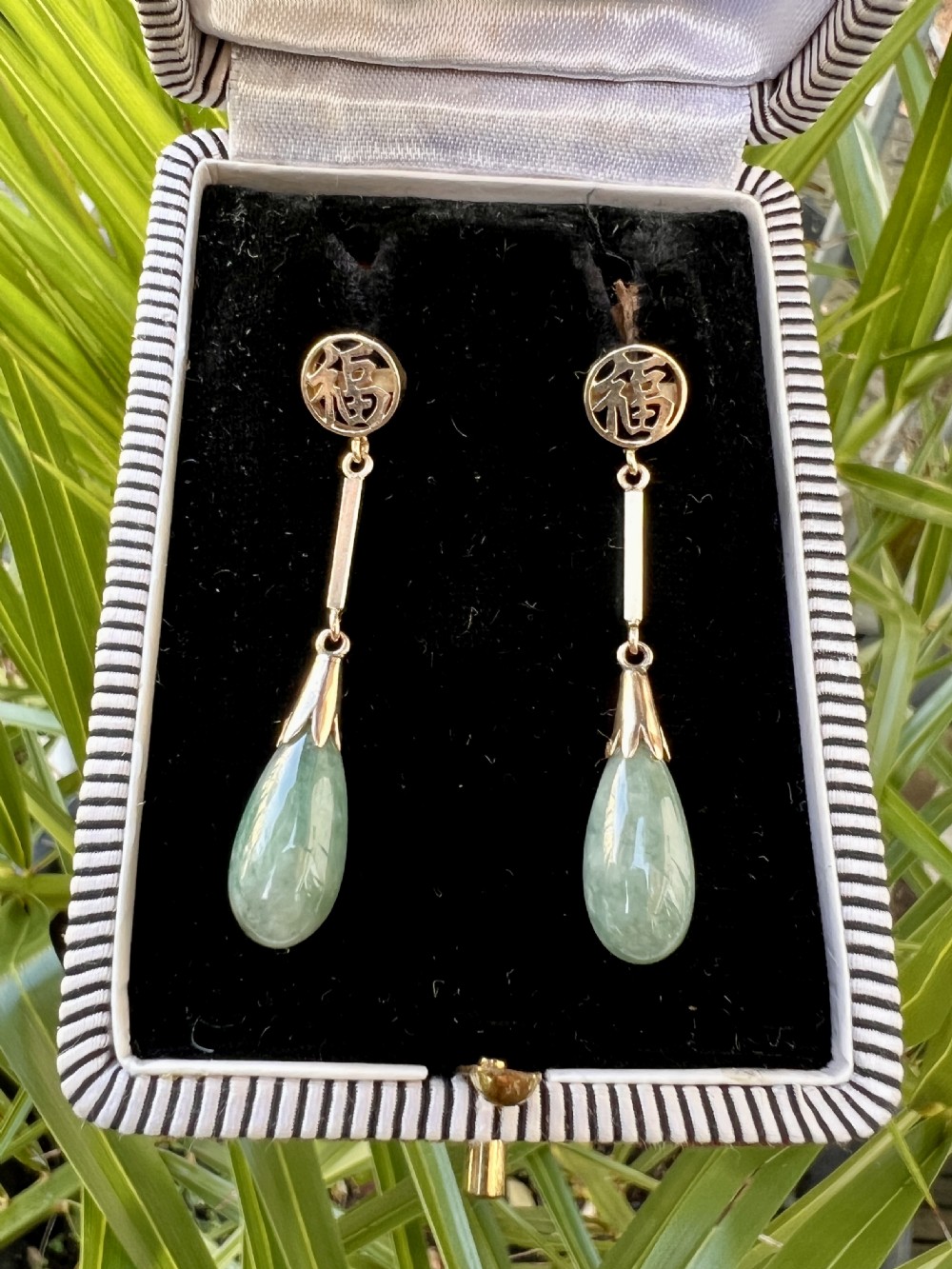 A pair of gold drop earrings featuring circular tops with pierced Chinese characters, slender gold bar links, and teardrop-shaped green jade stones. View VII