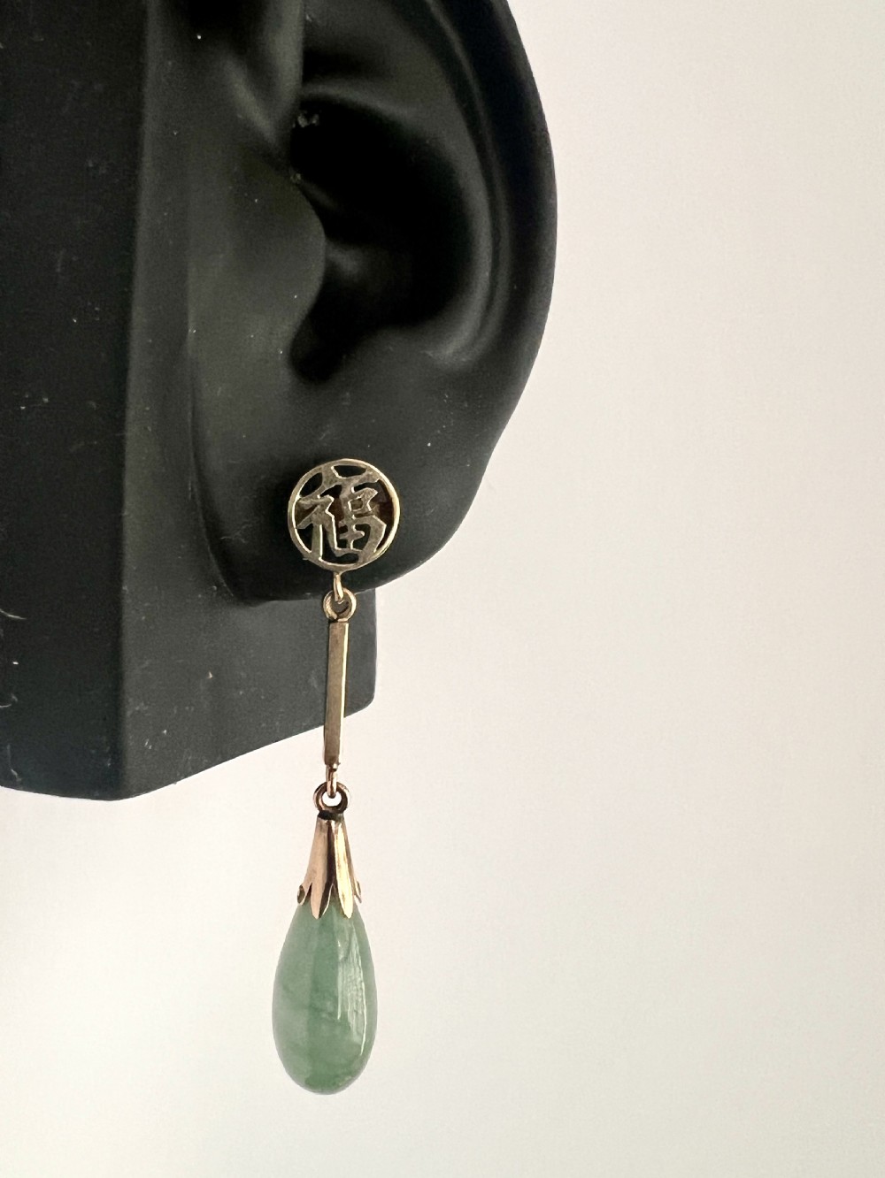 A pair of gold drop earrings featuring circular tops with pierced Chinese characters, slender gold bar links, and teardrop-shaped green jade stones. View VIII