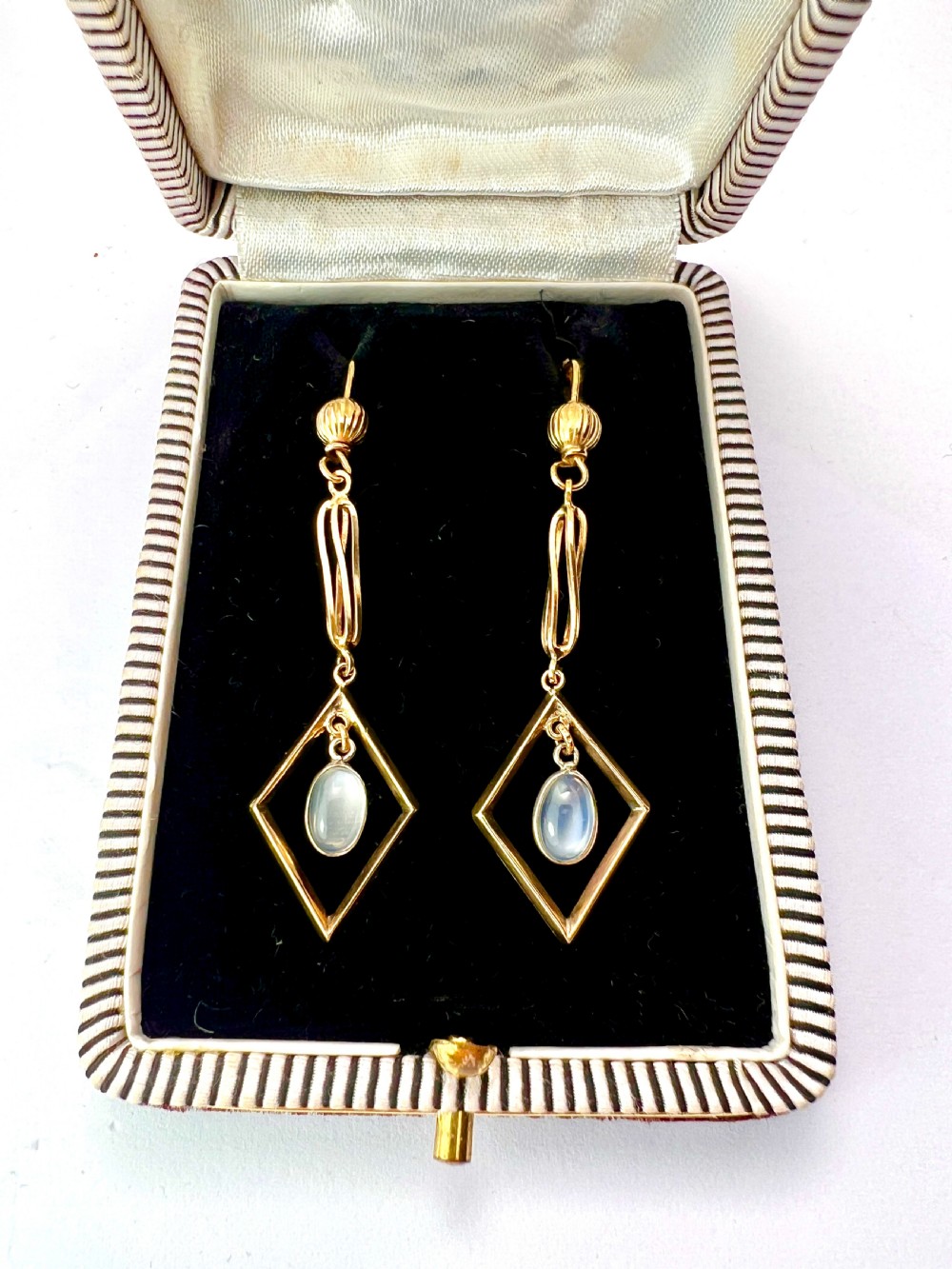 A pair of yellow gold drop earrings featuring ribbed shepherd hooks, linear twisted wire links, and open diamond-shaped frames containing oval moonstone cabochons. View IV