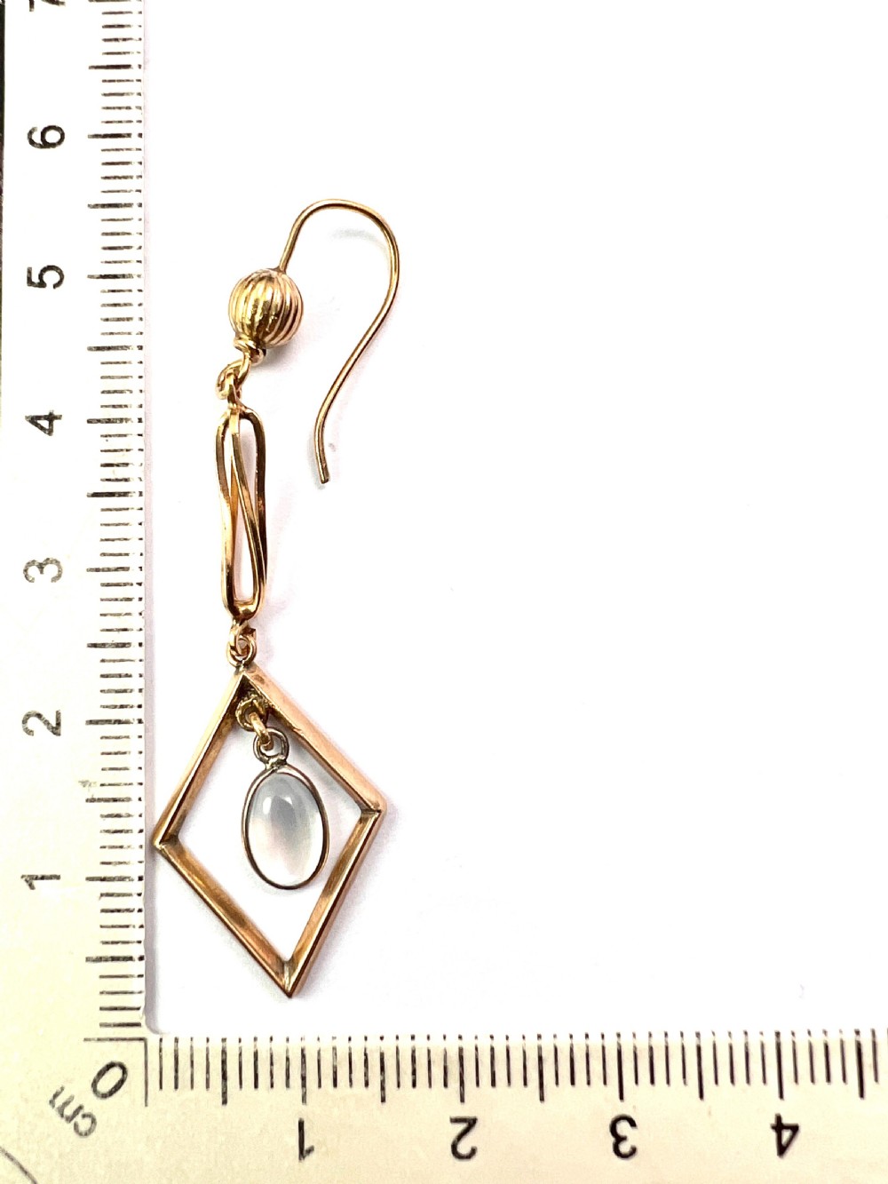 A pair of yellow gold drop earrings featuring ribbed shepherd hooks, linear twisted wire links, and open diamond-shaped frames containing oval moonstone cabochons. View VI