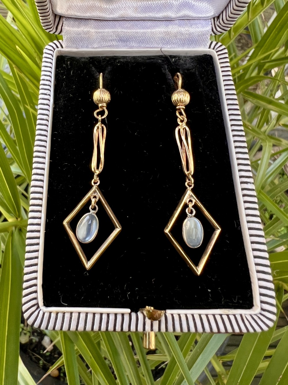 A pair of yellow gold drop earrings featuring ribbed shepherd hooks, linear twisted wire links, and open diamond-shaped frames containing oval moonstone cabochons. View VII