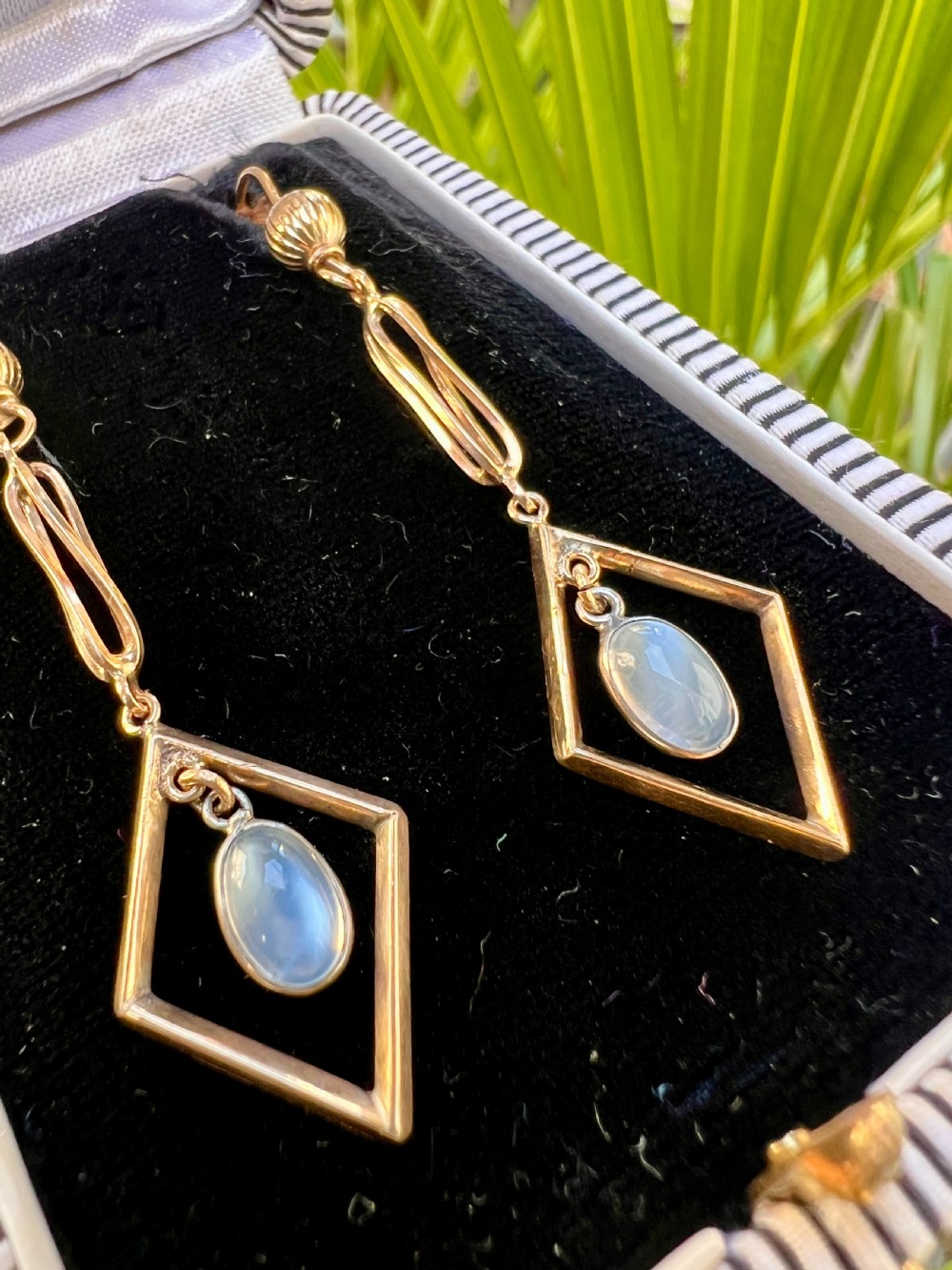 A pair of yellow gold drop earrings featuring ribbed shepherd hooks, linear twisted wire links, and open diamond-shaped frames containing oval moonstone cabochons. View VIII