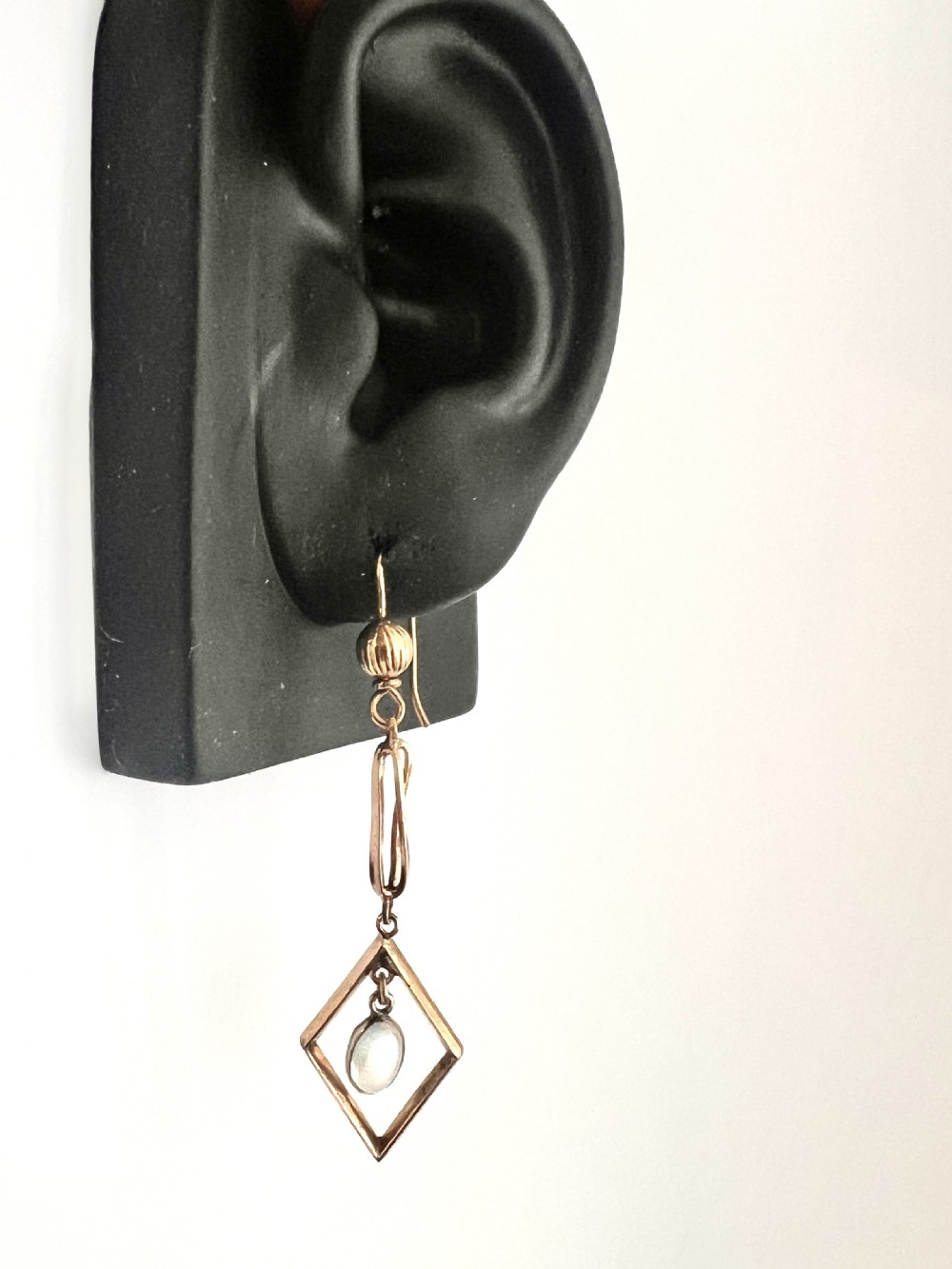 A pair of yellow gold drop earrings featuring ribbed shepherd hooks, linear twisted wire links, and open diamond-shaped frames containing oval moonstone cabochons. View IX