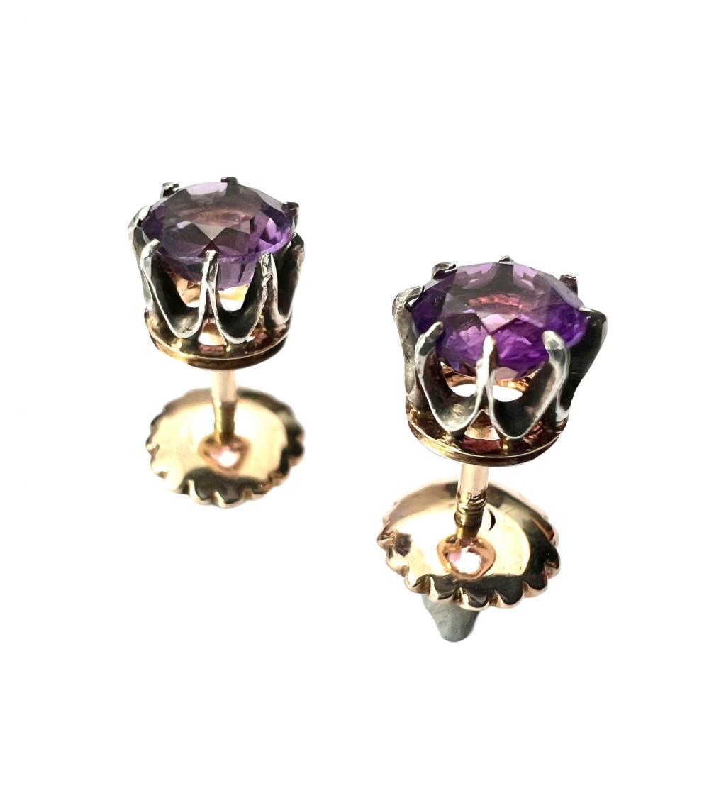 Pair of antique stud earrings featuring circular purple amethysts in multi-prong silver crown settings with yellow gold posts and scalloped backings.