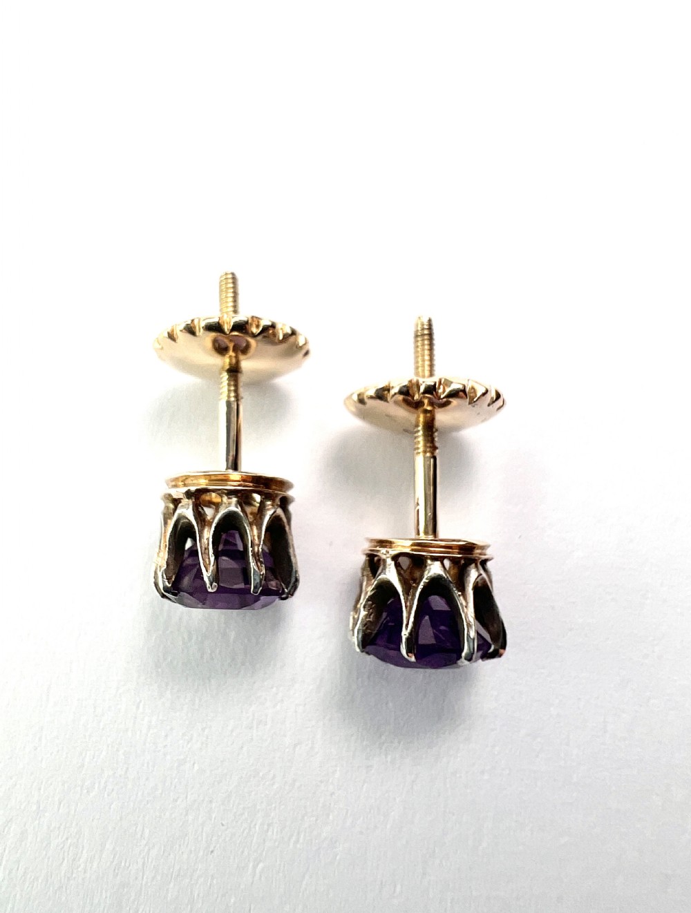 Pair of antique stud earrings featuring circular purple amethysts in multi-prong silver crown settings with yellow gold posts and scalloped backings. View II