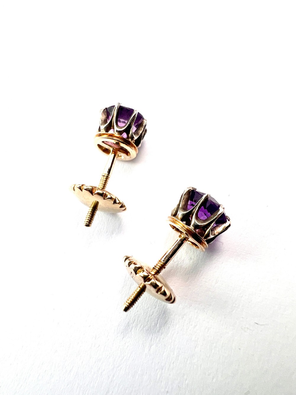 Pair of antique stud earrings featuring circular purple amethysts in multi-prong silver crown settings with yellow gold posts and scalloped backings. View VI