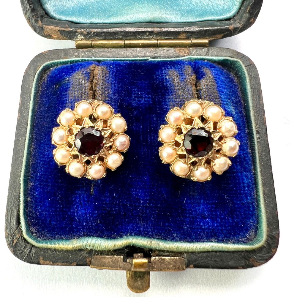A pair of Victorian gold cluster earrings featuring a central round faceted red garnet surrounded by seed pearls set in a starburst pattern.